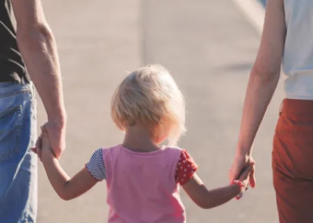 immagine di due adulti di spalle che conducono per mano una bambina